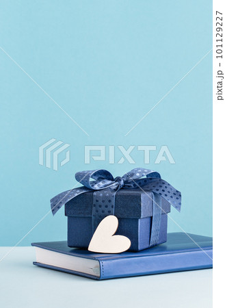 Small luxury gift box with blue bow agenda and white heart. Side view. Fathers day or Valentines day gift for him. Corporate thank you concept or birthday party. Festive sale copy space tall banner 101129227