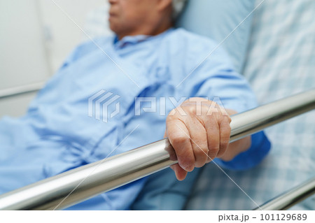 Asian elder senior woman patient holding bed rail while lie down with hope waiting her family in hospital. 101129689