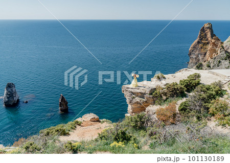 Woman in a yellow dress on the sea. Side view Young beautiful sensual woman in yellow long dress posing on a rock high above the sea at sunset. Girl in nature against the blue sky Woman in a yellow dress on the sea. Side view Young beautiful sensual woman in yellow long dress posing on a rock high above the sea at sunset. Girl in nature against the blue sky 101130189