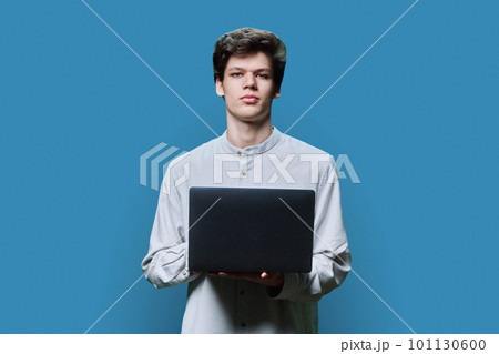 Portrait of young college student guy using laptop on blue background Portrait of young college student guy using laptop on blue background 101130600