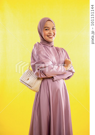 smiling muslimah woman wearing pink dress with bag on yellow smiling muslimah woman wearing pink dress with bag on yellow 101131144