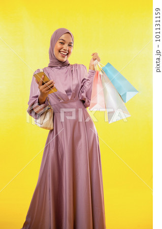 smiling feminine muslimah using mobile phone and carrying paper bag smiling feminine muslimah using mobile phone and carrying paper bag 101131159