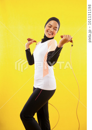 smiling Asian Muslim woman exercising skipping rope on a yellow smiling Asian Muslim woman exercising skipping rope on a yellow 101131198