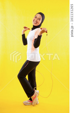 Side view of Muslim woman exercising skipping rope on yellow Side view of Muslim woman exercising skipping rope on yellow 101131265