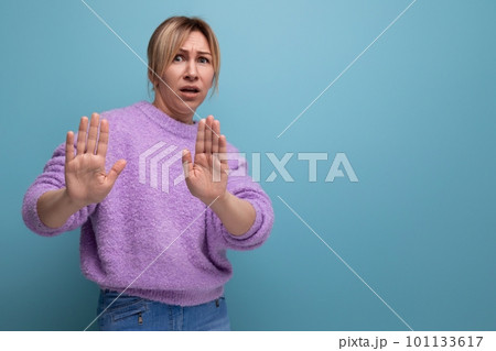 portrait of an indignant blonde young woman in a lavender sweater with a sign of denial on a bright portrait of an indignant blonde young woman in a lavender sweater with a sign of denial on a bright 101133617