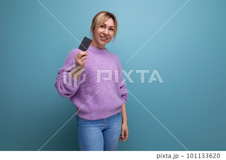 cute blond young woman consultant in purple hoodie holding credit plastic card mockup on blue 101133620