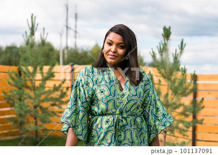 Summer portrait of beautiful african american woman in colourful dress wear standing on backyard. Suburban lifestyle and chilling on weekend in countryside and inclusion with diversity concept 101137091