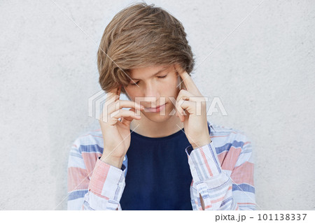Pensive concentrated teenage boy with stylish haircut looking down thinking over something important. Fashionable male holding fingers on temples trying to concentrate having very serious look 101138337