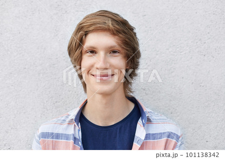 Handsome stylish schoolboy with trendy hairstyle wearing shirt looking with smile into camera having dark narrow eyes and thin lips. Fashionable young hipster guy having appealing appearance Handsome stylish schoolboy with trendy hairstyle wearing shirt looking with smile into camera having dark narrow eyes and thin lips. Fashionable young hipster guy having appealing appearance 101138342