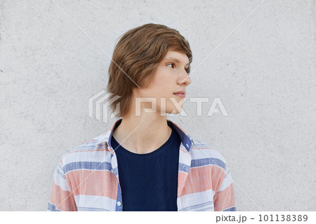 Portrait of teenage boy with trendy hairstyle wearing T-shirt and shirt looking away having deep thoughts while standing over white concrete wall. Serious hipster guy isolated over white background Portrait of teenage boy with trendy hairstyle wearing T-shirt and shirt looking away having deep thoughts while standing over white concrete wall. Serious hipster guy isolated over white background 101138389