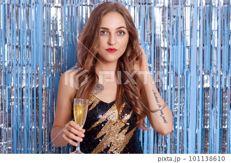 Portrait of beautiful young woman in beautiful cocktail black dress, girl holding glass with wine or champagne in her hands, posing against white background. 101138610