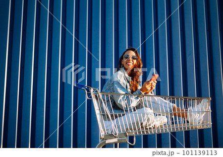 Young woman with shopping cart having fun near color wall. smilling african woman going shopping. 101139113