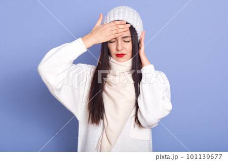 Horizontal indoor picture of exhausted ill sweet young lady closing eyes, putting hand on forehead, having fever, putting hand on ear, having earache, feeling bad. People and health concept. 101139677