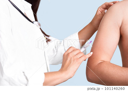 Close up shot of female doctor`s hands makes vacciantion to patient, uses syringe, inject at upper arm, prevents serious disease, isolated over blue background. Selective focus. Heathcare concept 101140260