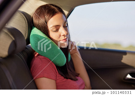 Fatigue brunette woman uses green pillow for travelling in car, has tired look, dressed in casual t shirt, poses in automobile, falls asleep. People, tourism and journey concept. Female enjoys comfort 101140331