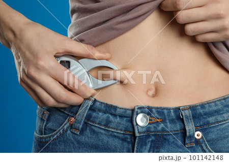 Young woman measuring body fat with caliper on blue background, closeup 101142148