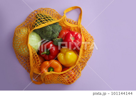 Net bag with vegetables on lilac background, top view 101144144