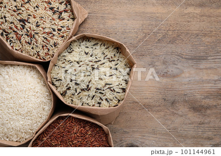 Different types of brown and polished rice in paper bags on wooden table, flat lay. Space for text Different types of brown and polished rice in paper bags on wooden table, flat lay. Space for text 101144961