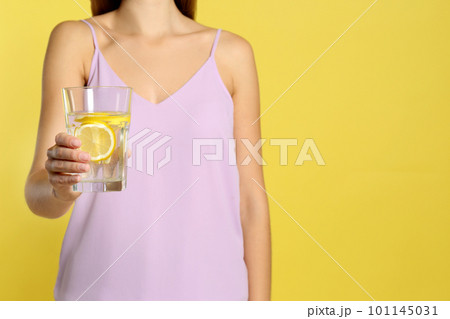 Young woman with glass of lemon water on yellow background, closeup. Space for text Young woman with glass of lemon water on yellow background, closeup. Space for text 101145031