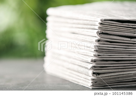 Stack of newspapers on grey table against blurred green background, closeup. Journalist's work 101145386