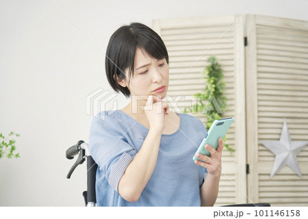 リビングでスマホを使いながら考える車椅子に乗った女性 リビングでスマホを使いながら考える車椅子に乗った女性 101146158