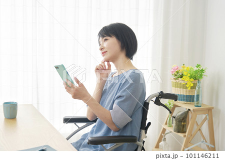 リビングでスマートフォンを使いながら想像する車椅子に乗った女性 リビングでスマートフォンを使いながら想像する車椅子に乗った女性 101146211