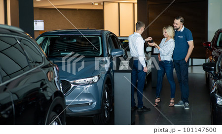 The seller hands over the car keys to the buyers. The couple bought a new car. 101147600