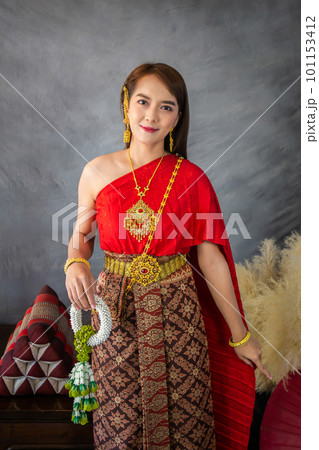 young woman wearing a original traditional red Thai dress and golden ornaments stands holding a jasmine garland. Thai national costume young woman wearing a original traditional red Thai dress and golden ornaments stands holding a jasmine garland. Thai national costume 101153412