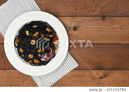 Black seafood pasta in white plate over linen towel on rustic background . Black Mediterranean spaghetti on wood background with copy space. Black seafood pasta in white plate over linen towel on rustic background . Black Mediterranean spaghetti on wood background with copy space. 101153784