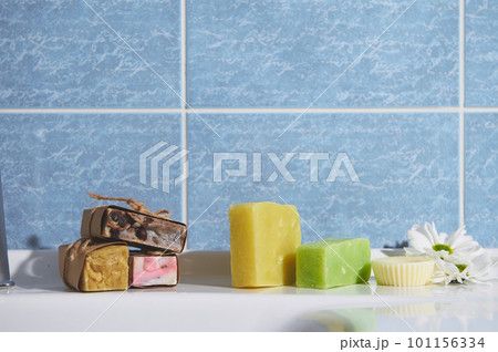 Still life with organic cold pressed soap bars with herbal ingredients and essential oils, for purity, home spa, skin and body care, on the bathroom wash basin against blue marble wall background 101156334