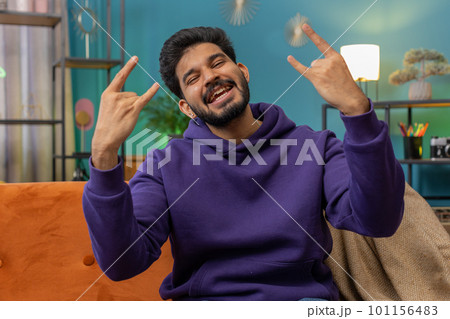 Overjoyed indian man showing rock n roll gesture cool sign dancing rejoicing in success at home room Overjoyed indian man showing rock n roll gesture cool sign dancing rejoicing in success at home room 101156483