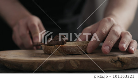 man spreading chocolate hazelnut spread on ciabatta slice on wood board 101163223