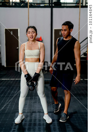 Asian sport woman hold weight to exercise with support by the trainer in fitness gym. 101164845
