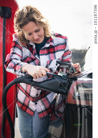 Woman in a plaid shirt charging an electric car 101167396