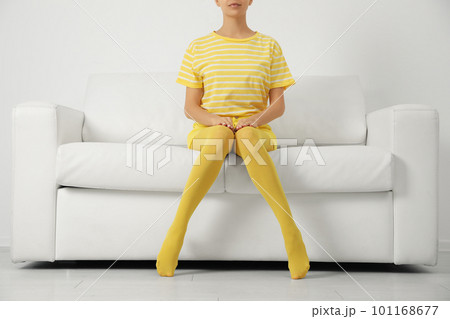 Woman wearing yellow tights sitting on sofa indoors, closeup 101168677