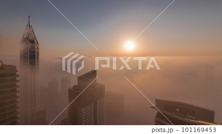 Rare early morning winter fog above the Dubai Marina skyline and skyscrapers lighted by sun aerial timelapse. 101169453