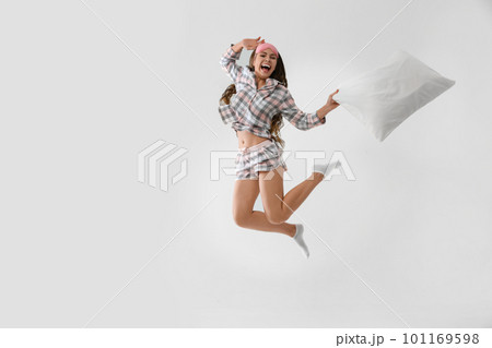 Beautiful woman with pillow jumping on light grey background. Bedtime Beautiful woman with pillow jumping on light grey background. Bedtime 101169598