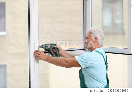 Mature construction worker repairing plastic window with electric screwdriver indoors Mature construction worker repairing plastic window with electric screwdriver indoors 101169642