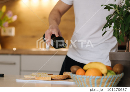 Close-up of man spreads olive oil on baguette. Bright kitchen interior Close-up of man spreads olive oil on baguette. Bright kitchen interior 101170687
