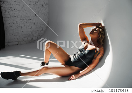 a portrait of a sexy blonde with tattoos in a leather swimsuit and boots. 101173453