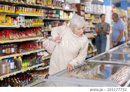 Old woman purchaser choosing frozen product in big supermarket Old woman purchaser choosing frozen product in big supermarket 101177732