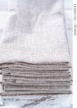 Closeup view of a natural color linen dinner napkin on a wooden white table. Closeup view of a natural color linen dinner napkin on a wooden white table. 101180541