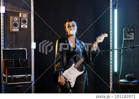Brunette rockstar woman with short hair and grunge style blowing bubble gum while playing electric guitar preparing for rock concert. Guitarist using electric instrument to performing heavy music Brunette rockstar woman with short hair and grunge style blowing bubble gum while playing electric guitar preparing for rock concert. Guitarist using electric instrument to performing heavy music 101182071