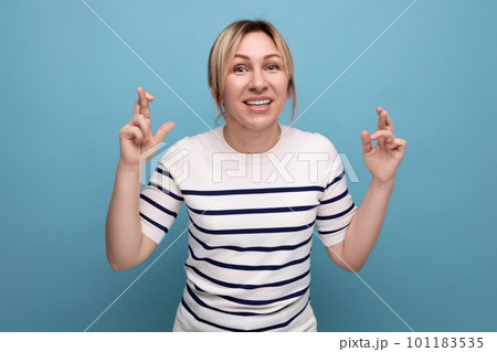 close-up photo of a blond young woman crossing her fingers and praying on a blue background with close-up photo of a blond young woman crossing her fingers and praying on a blue background with 101183535