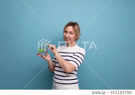 cute blond young mother showing shopping cart miniature on blue background with copy space 101183700