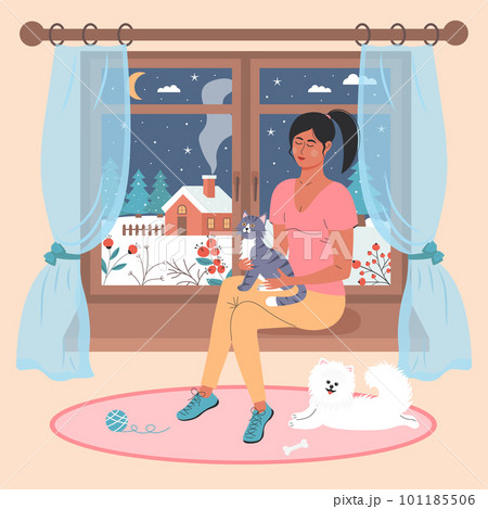 Girl with a cat sitting on the window. White spitz lying on the rug nearby. There is a winter night landscape outside the window. Winter mood, love pets, relaxing, cozy home concept. 101185506