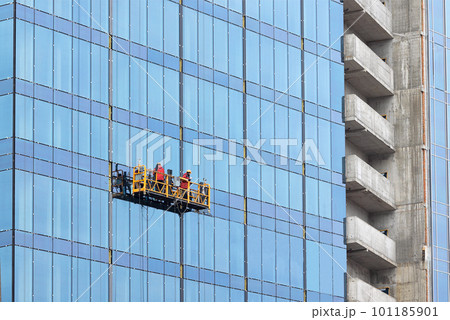 Construction workers on a suspended cradle mount the glass facade of a multi-story skyscraper. 101185901