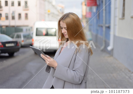 girl with red hair in coat looks something in a tablet on a city girl with red hair in coat looks something in a tablet on a city 101187373