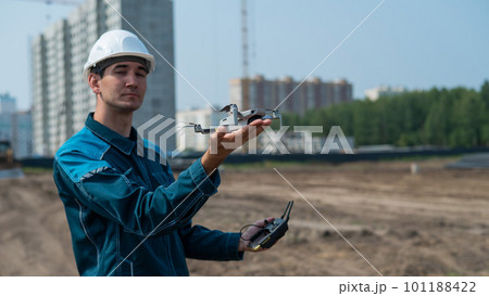 A man in a helmet and overalls controls a drone at a construction site. The builder carries out technical oversight. A man in a helmet and overalls controls a drone at a construction site. The builder carries out technical oversight. 101188422