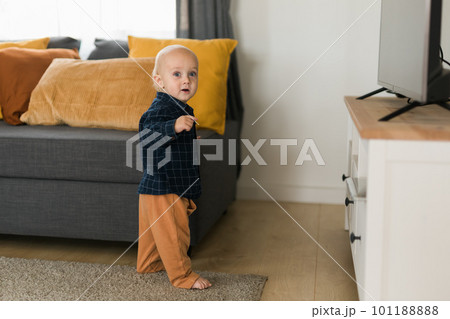 Toddler boy laughing having fun standing near sofa in living room at home copy space. Adorable baby making first steps alone. Happy childhood and child care concept Toddler boy laughing having fun standing near sofa in living room at home copy space. Adorable baby making first steps alone. Happy childhood and child care concept 101188888